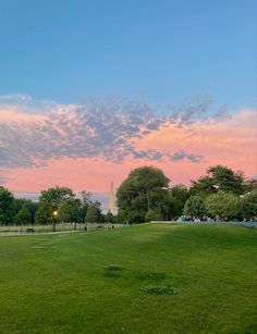 the washington monument at sunset with pink clouds in the sky and green grass on the ground