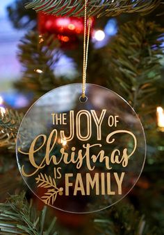 the joy of christmas is family ornament hanging from a christmas tree with lights in the background