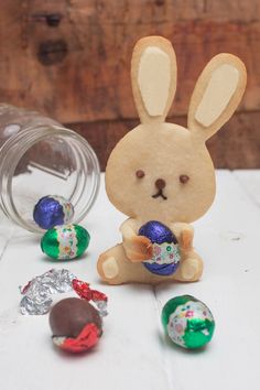 a bunny holding an easter egg next to some chocolate eggs on a white table with wood background