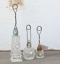 three glass vases with metal handles on a wooden table next to a white wall