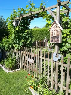 a bird house is hanging on a wooden trellis in the grass near a fence