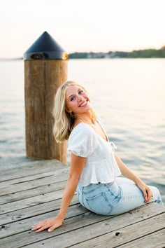 a beautiful blonde woman sitting on top of a wooden dock