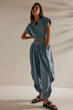 a woman standing in front of a white wall with her hands on her hips wearing sandals