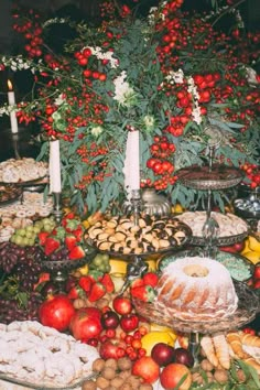 an assortment of fruits and pastries on a table with candles in the background,