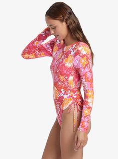 Made of VITA Xtra life Lycra recycled fabric (so it won't stretch out or fade), the Sunrise Tides printed long-sleeve swimsuit has an eye-catching open back design, skimpy bum coverage, and a high-leg cut complete with ruching and side-ties. Bonus? It's chlorine resistant and offers high sun protection. Stretch Floral Print Swimwear For Surfing, Long Sleeve Floral Print Stretch Swimwear, Tropical Long Sleeve Swimwear For Pool, Fitted Printed Rash Guard For Beach, Fitted Printed Rash Guard For The Beach, Long Sleeve Floral Print Swimwear For Surfing, Tropical Long Sleeve Fitted Swimwear, Fitted Long Sleeve Tropical Swimwear, Fitted Printed Rash Guard For Poolside