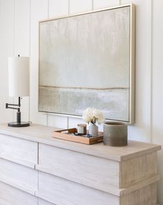 a white dresser with flowers on top and a large painting above it