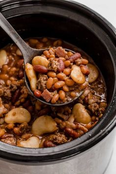 a ladle full of beans and meat in a slow cooker with a spoon