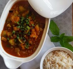 there is a bowl of stew and rice on the table next to it, along with a spoon