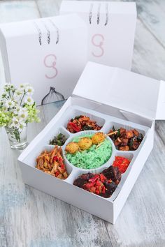 two white boxes filled with different types of food on top of a wooden table next to flowers