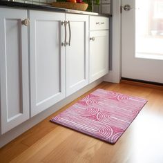 a kitchen with white cabinets and pink rug on the wooden floor next to the sink