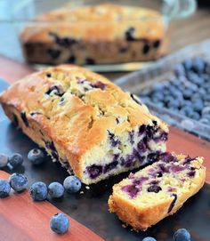 a loaf of blueberry bread sitting on top of a cutting board next to sliced blueberries