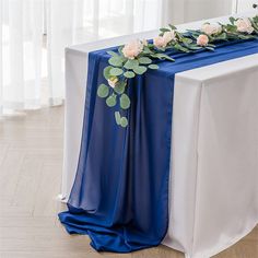 a blue table runner with white flowers and greenery on the top is ready to be served