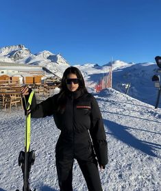 a woman standing on top of a snow covered ski slope holding onto her skis