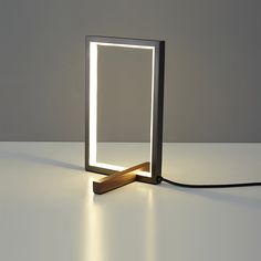 a square light sitting on top of a table next to a wooden object with a long cord