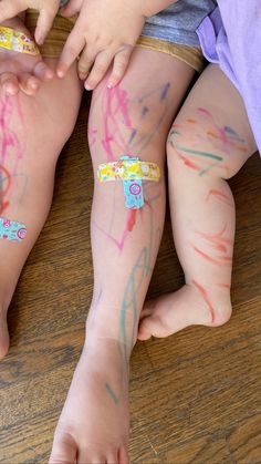 two children with their hands on each other's legs covered in colorful paint and writing