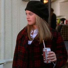 a woman with a drink in her hand and a hat on is walking down the street