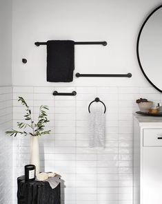 a bathroom with white tiles and black accessories on the wall, along with a round mirror