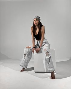 a woman sitting on top of a white chair wearing ripped jeans and a bandana