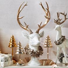 two white deer statues sitting on top of a table next to christmas trees and presents