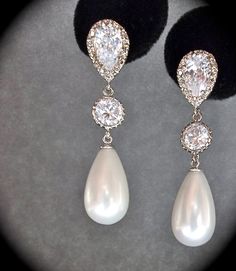 two pairs of white pearl and diamond earrings on display in front of a black background