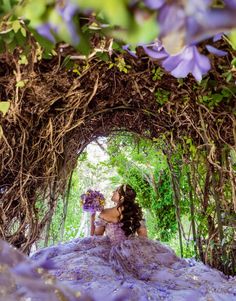 a woman in a purple dress is sitting under an arch with vines and flowers on it