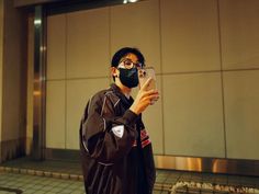 a man wearing a face mask taking a selfie with his cell phone in front of a building