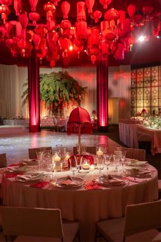 a table set up for a formal dinner with red lights and chandeliers hanging from the ceiling