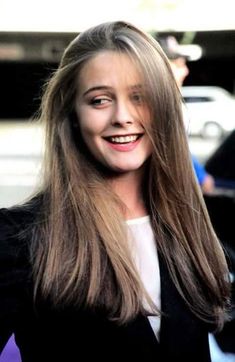 a woman with long hair is smiling at the camera while wearing a black blazer and white shirt