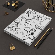 an open notebook with black and white video game controllers on it, surrounded by gold objects