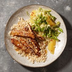 a white plate topped with rice and meat next to a side of salad on a table