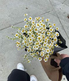 someone holding a bouquet of daisies on the sidewalk