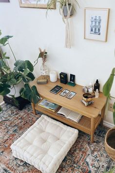 a living room with plants and books on the coffee table next to a footstool