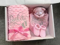 a pink baby gift set in a box with a teddy bear and booties on it