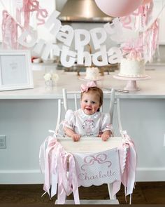 a baby sitting in a highchair at a table with pink and white decorations