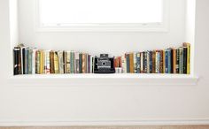 a bookshelf filled with lots of books next to a white window sill