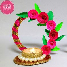 a small decorative item with flowers and pearls on it's edge, sitting next to a lit candle