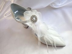 This elegant shoe is a leather handmade high pointed wedding court shoe, using ostrich feathers and a light-catching crystal buckle on an organza flower that sweeps attractively along the foot, creating the most elegant effect. The luxurious leather lining is cushioned in all the right places to ensure ultimate comfort. These beautiful shoes are the perfect finishing touch with any bridal outfit. Genuine white leather Pointed toe Block heel Ankle strap Leather lining Leather sole Heel height mea Wedding Block Heels, Heels For Bride, Feather Shoes, Shoes For Bride, White Bridal Shoes, Bridal Pumps, Boho Jewels, Jeweled Shoes, Wedding Pumps