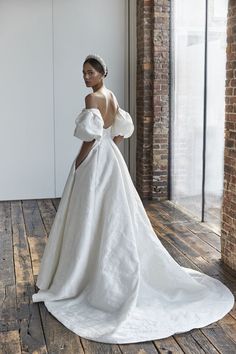 a woman in a white dress standing on a wooden floor next to a brick wall