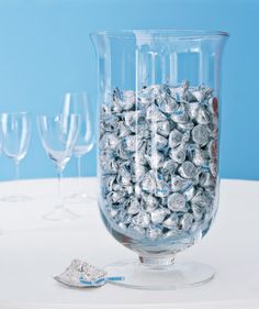 a glass vase filled with silver foiled candy next to wine glasses on a table