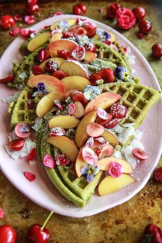 a white plate topped with waffles covered in fruit and toppings next to cherries