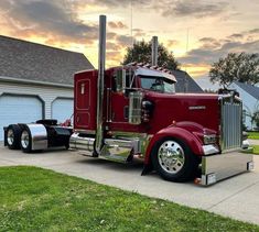 a large red semi truck parked in front of a house with a sunset behind it