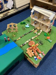 a toy house sitting on top of a fake grass covered field with toys around it