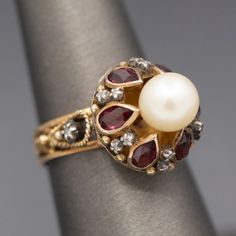 Glowing Rhodolite Garnet Cultured Pearl and Diamond Slice Mid Century Georgian Revival Statement Ring in 14k Yellow Gold Crafted in mid-century with definite nods to Georgian design, this ring features a gorgeous glowing pearl atop bezel set rhodolite garnets separated by tiny diamond slices. The pearl is cultured and measures 7.41mm, with an ivory color and strong reflections. There are six of the rhodolite garnets- red with a pinkish hue. The garnets measure about 5 x 3mm, calculating to 0.15c Georgian Design, Georgian Revival, Pearl Cocktail Ring, Garnet And Diamond Ring, Ruby Rings, Rose Gold Accents, Garnet Jewelry, Celestial Jewelry, Tiny Diamond