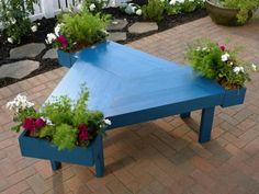 a blue table with flowers in it on a brick walkway next to a white picket fence