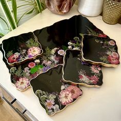 four black plates with flowers on them sitting on a counter