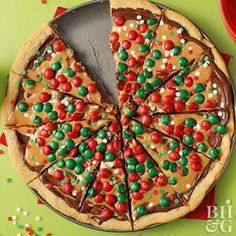 a pizza with chocolate and candy toppings on a green table next to confetti sprinkles