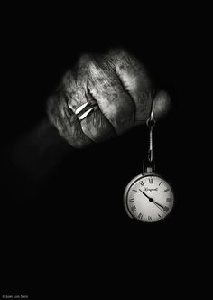 an old hand holding a pocket watch in the dark