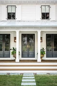 a white house with black doors and steps leading up to the front door that has green trim