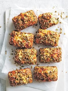 six pieces of bread with nuts and seeds on it sitting on a piece of parchment paper