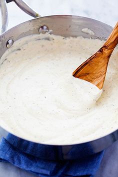 a wooden spoon in a pan filled with white sauce on top of a blue towel